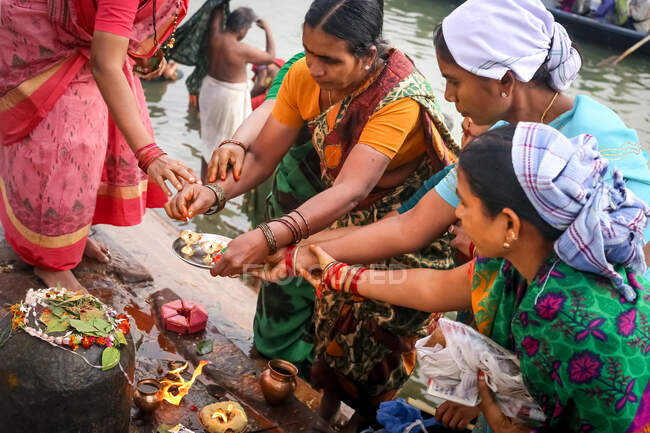 INDIA, VARANASI - NOVEMBRE 2o, 2015: Dall'alto gruppo di donne etniche nelle donne asiatiche tradizionali in abiti tradizionali indiani che pregano e fanno offerte con candele e fiori vicino al fiume in India — Foto stock