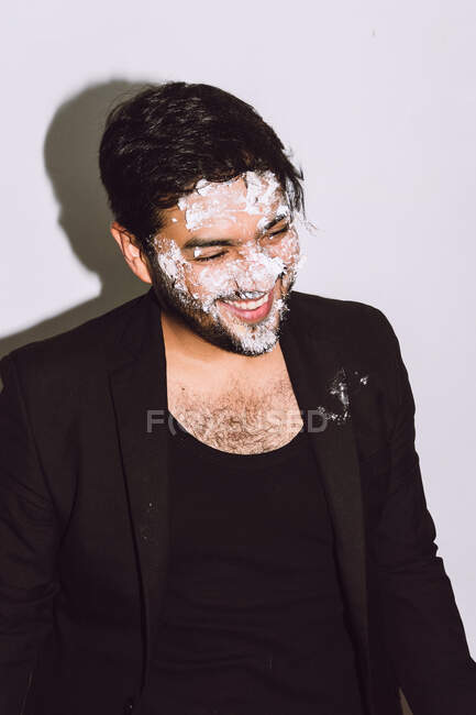 Hombre feliz con la cara sucia riendo con la boca abierta después de pastel de cumpleaños roto en el estudio - foto de stock