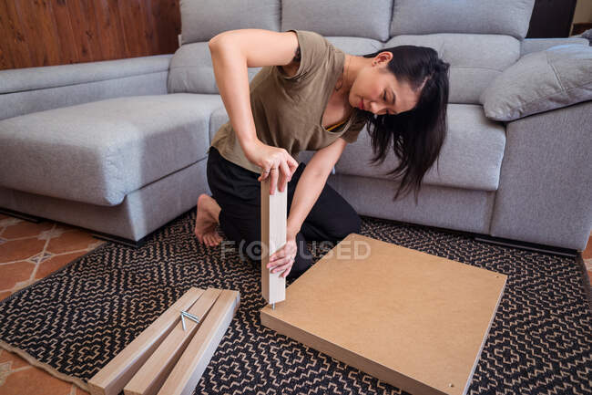 Focused young Asian female attaching table leg to tabletop on ornamental carpet in light house — Stock Photo