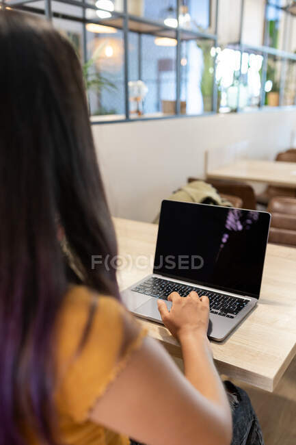 Back view of unrecognizable young female entrepreneur sitting at table and browsing netbook while working on modern workplace — Stock Photo