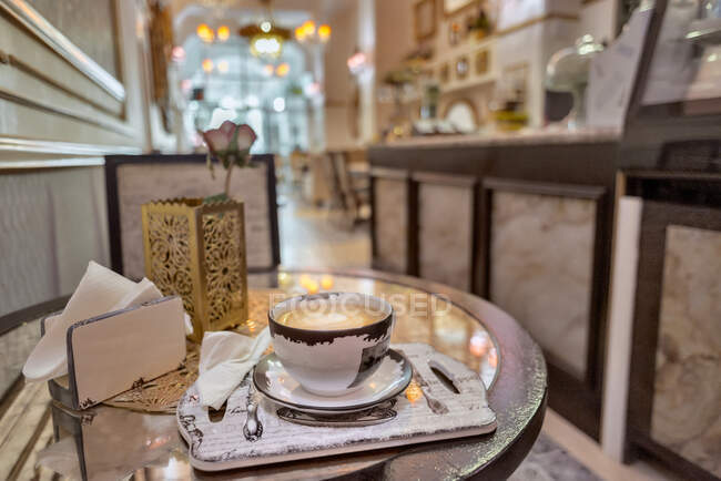 Taza de cerámica de café aromático con latte arte en la mesa con servilletas y rosa en flor en la cafetería - foto de stock