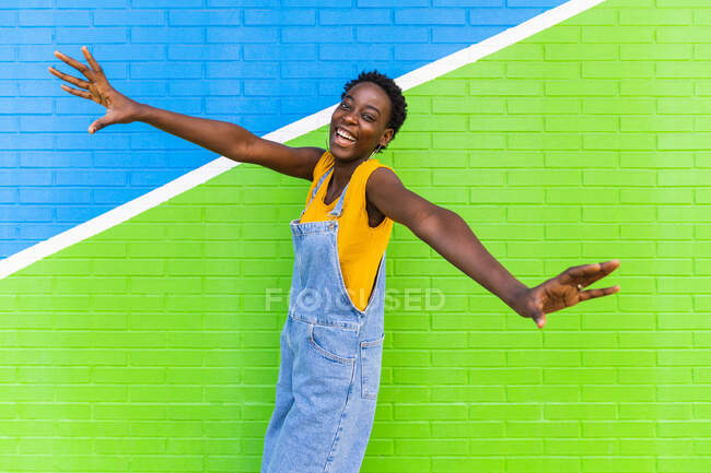 Seitenansicht einer fröhlichen Afroamerikanerin, die beim Sprung über den Boden in der Nähe einer hellen Mauer lächelt — Stockfoto