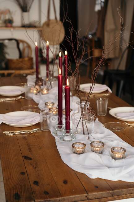Tovaglia bianca e piatti disposti su tavolo festivo decorato con candele ardenti e rami secchi di albero — Foto stock