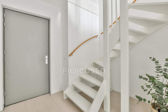 Интерьер просторного светлого коридора с белой лестницей в квартире с минималистичным дизайном — стоковое фото