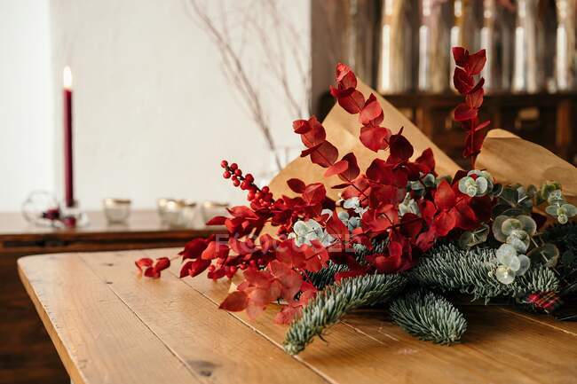 Festive stylish decorative Christmas bouquet with twigs of eucalyptus and bright red branches with berries placed on wooden table in room — Stock Photo