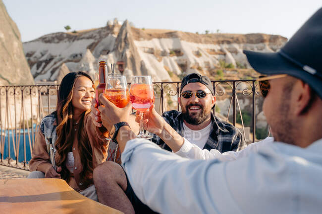 Smiling friends sitting around table and raising glasses of cocktails while hanging out in bar — Stock Photo