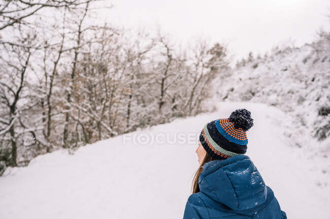 Back view of unrecognizable female traveler in warm outerwear walking on pathway in snowy woods in winter day — Stock Photo