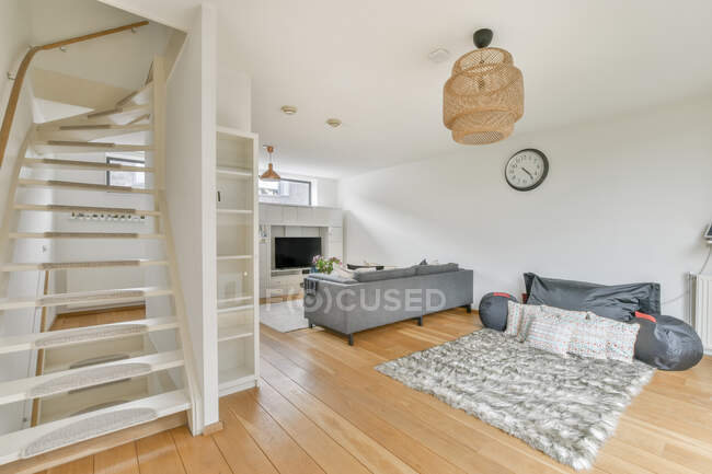 Креативный дизайн гостиной с диваном между телевизором и мягким ковром на фоне лестницы в доме — стоковое фото