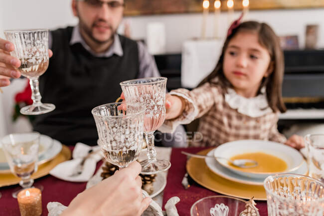 Crop father and daughter clinking glasses of alcoholic drink against unrecognizable mother at table during New Year holiday at home — Stock Photo