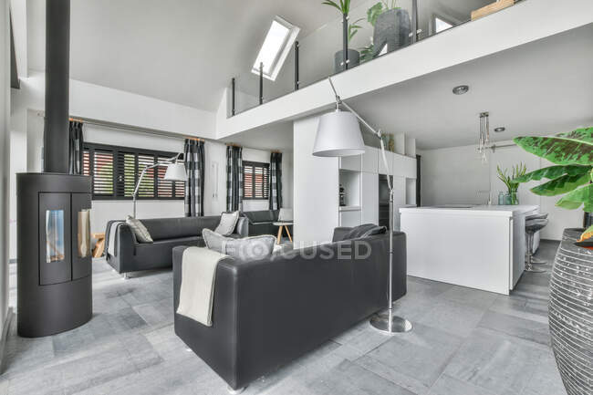 Интерьер стильной просторной гостиной серого цвета с удобными диванами против современной кухни — стоковое фото