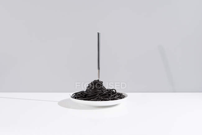Forchetta inox in ciotola piena di spaghetti neri con inchiostro di seppia su tavolo bianco in studio su sfondo grigio — Foto stock