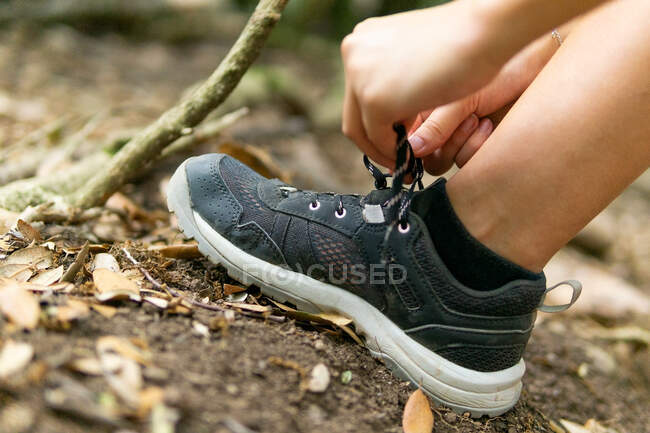 Crop excursionista anónimo atando cordones de zapatillas de deporte mientras camina en los bosques y explorar la naturaleza - foto de stock