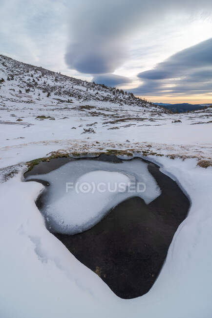 Landscape of snowy slope of hill in highland under cloudy sky in daylight and a puddle of ice water — Stock Photo