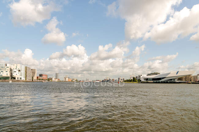 Museum und Kino EYE Film Institute in der Nähe von modernem Turm und im Bau befindlichem Gebäude an der Küste des reißenden Flusses in Amsterdam — Stockfoto