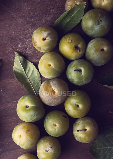 From above of fresh ripe plums and green leaves placed on wooden table in daytime — Stock Photo