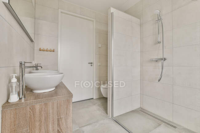 Cabina de ducha de luz frente a lavabos y espejo en elegante baño en apartamento moderno - foto de stock