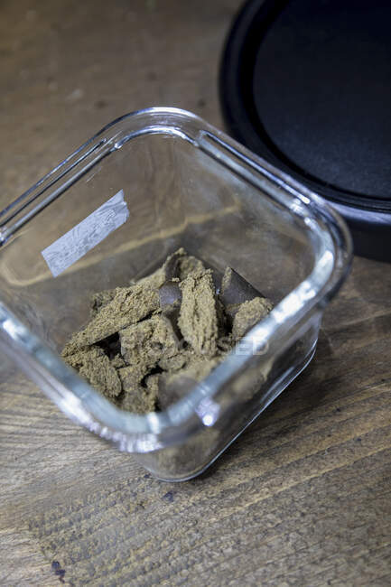 Dried hemp flower buds in transparent container on wooden table in room on blurred background — Stock Photo