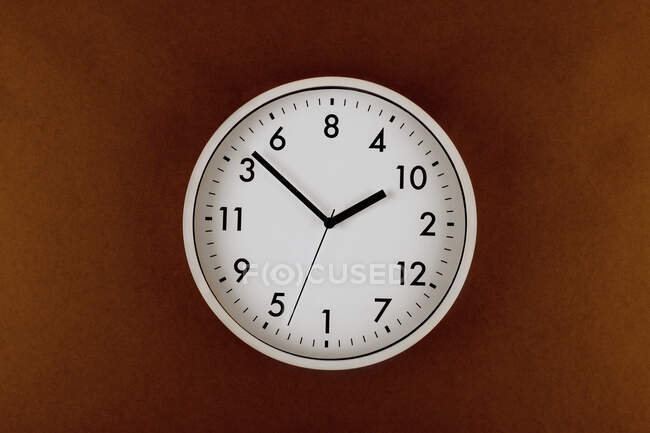 Round shaped minimalistic clock with numbers and arrows on colorful brown background — Stock Photo