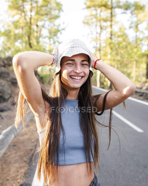 Aufrichtige Teenagerin mit langen Haaren und Händen hinter dem Kopf, die an einem sonnigen Tag auf Teneriffa in die Kamera schaut — Stockfoto