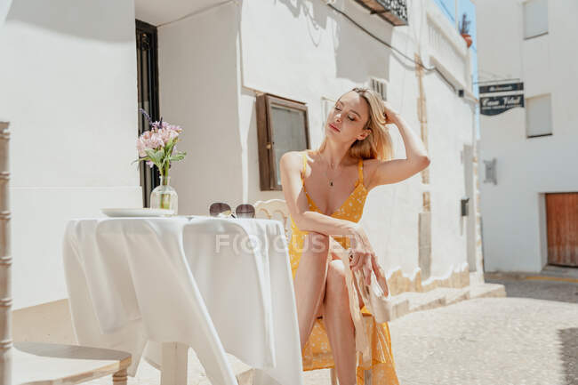 Ballerine féminine paisible avec les yeux fermés attachant les cheveux tout en étant assis à table avec des jambes croisées et des chaussures pointes dans la vieille ville — Photo de stock