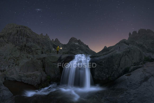 Voyageur admirant cascade avec mousse sur monture rugueuse contre étang sous le ciel étoilé au crépuscule — Photo de stock