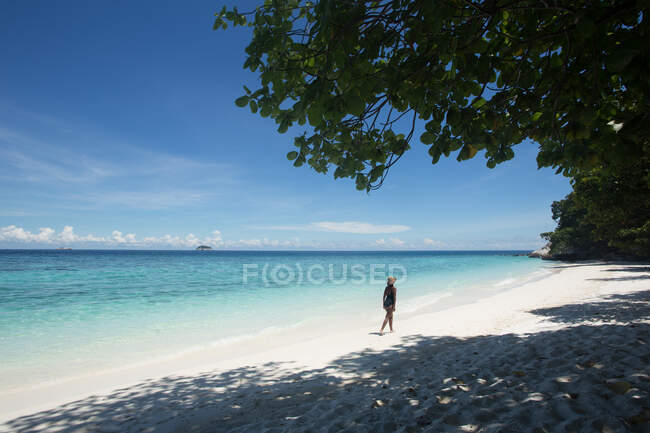 Обратно посмотреть этнических женщин-туристок в купальниках и соломенной шляпе, идущих по песку во время поездки в Малайзию — стоковое фото