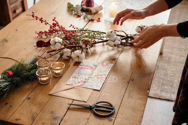 De cima da colheita pessoa irreconhecível que trabalha na mesa de madeira com cartão postal e buquê decorativo — Fotografia de Stock