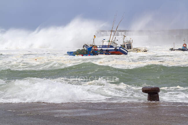 Navi moderne galleggianti in acqua di mare schiumosa con potenti onde e spruzzi vicino alla costa nel porto di Cudillero nelle Asturie Spagna — Foto stock