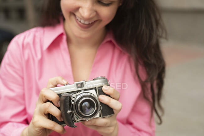 Обрізана молода щаслива жінка з довгим коричневим волоссям фотографує стару модну фотокамеру на вулиці міста — стокове фото