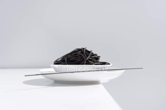 De cima de tigela de cerâmica com espaguete delicioso com tinta de lula preta com pauzinhos no fundo cinza — Fotografia de Stock