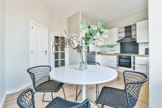 Espaçosa cozinha leve com armários brancos e zona de jantar mobilada com mesa branca e cadeiras — Fotografia de Stock