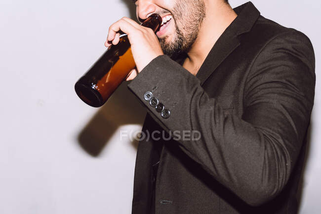 Cosecha alegre irreconocible macho con los ojos cerrados bebiendo cerveza de la botella durante la fiesta sobre fondo blanco - foto de stock