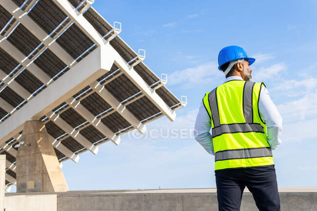 Low angle back view of unrecognizable male inspector in vest with protective helmet against modern solar power station — Stock Photo