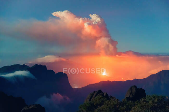 Paisagem noturna com um vulcão em erupção no fundo e um mar de nuvens cobrindo as montanhas de uma montanha vegetada e rochosa. Erupção vulcânica Cumbre Vieja nas Ilhas Canárias de La Palma, Espanha, 2021 — Fotografia de Stock