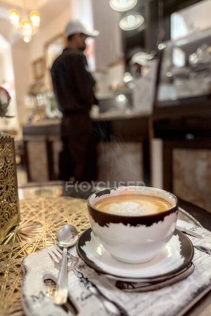 Керамічна чашка ароматичної кави з лате-мистецтвом на столі з серветками і квітучими трояндами в кафетерії. — стокове фото