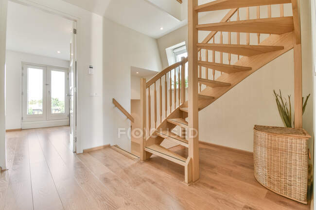 Design criativo do interior da casa com escadaria curva e cesta de palha no chão de madeira durante o dia — Fotografia de Stock