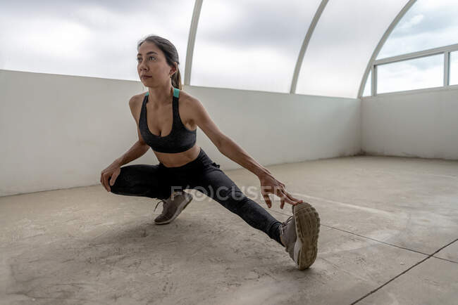 Joven deportista étnica flexible en desgaste activo estiramiento de la pierna durante el entrenamiento durante el día - foto de stock