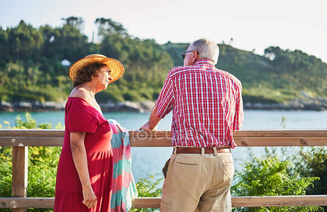 Seniorenpaar steht dicht beieinander und schaut sich an, während es bei sonnigem Wetter den Blick aufs Meer genießt — Stockfoto