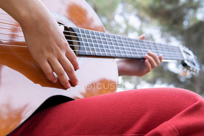 Crop unrecognizable female teenager playing classic guitar while having spare time in park in daylight — Stock Photo