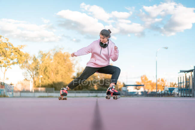Corpo inteiro de skatista jovem ativo vestindo capuz rosa e jeans pretos com patins praticando habilidades no parque de skate — Fotografia de Stock
