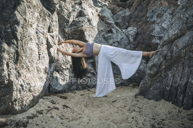 Flexível jovem etnia feminina realizando backbend enquanto se equilibra em uma perna durante a prática de ioga entre montagens — Fotografia de Stock