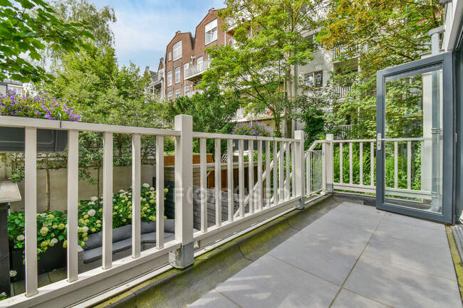 Balcone recintato con porta aperta contro la facciata dell'edificio di abitazione e alberi verdi nel patio durante la giornata estiva — Foto stock