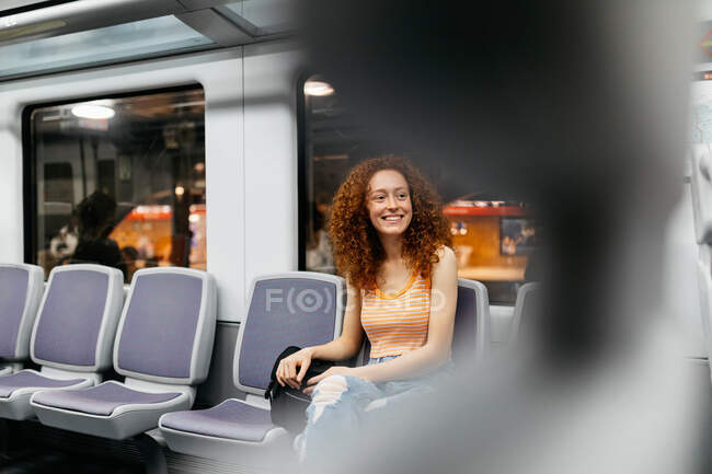Mujer joven contenta en jeans rasgados con pelo rojo rizado viajando en tren - foto de stock