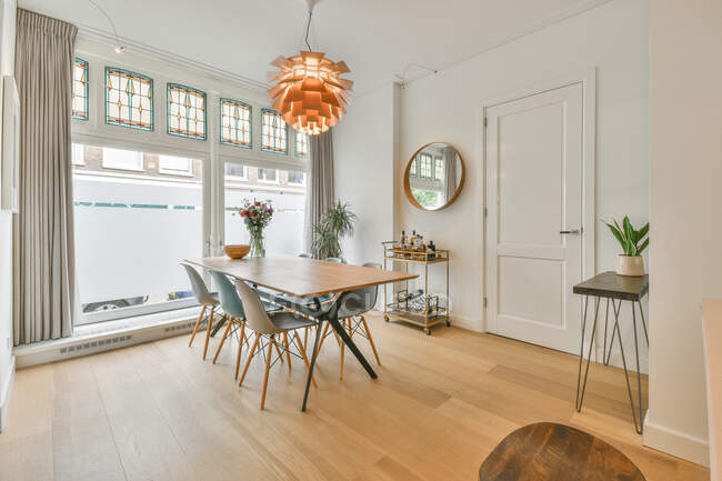 Современный интерьер столовой с деревянным столом и пластиковыми стульями под креативной люстрой в просторной новой квартире — стоковое фото