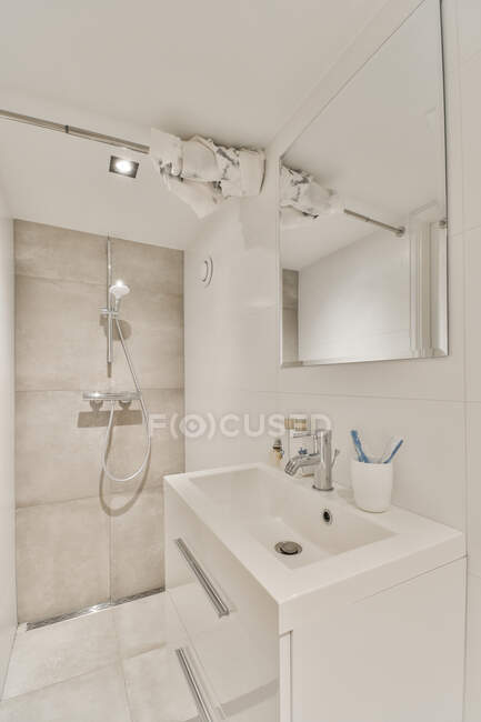 Interior moderno do banheiro com lavatório de cerâmica sob espelho contra chuveiro com lâmpada em casa — Fotografia de Stock
