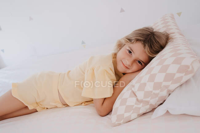 Kind cute child looking at camera while lying on bed at home — Stock Photo