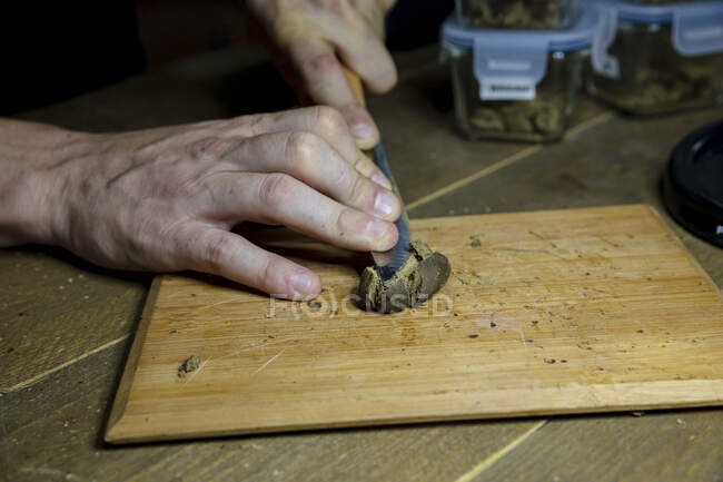 Cultivez un mâle méconnaissable avec un couteau écrasant une plante de cannabis séchée sur une planche de bois dans un espace de travail — Photo de stock