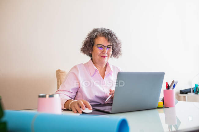 Female senior entrepreneur with tablet and netbook working at desk with graphics on paper sheets — Stock Photo