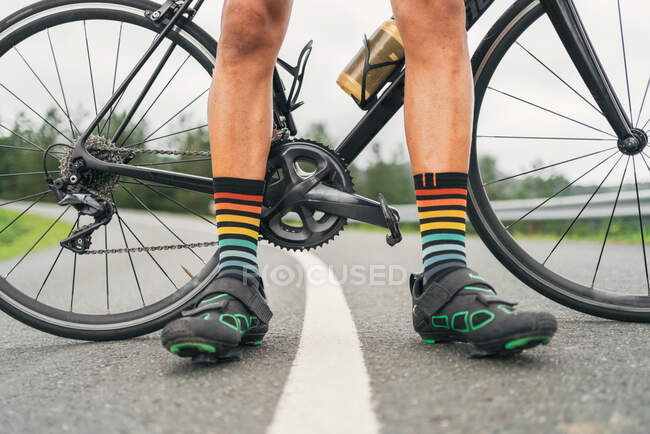 Ground level of faceless male athlete in cycling shoes and striped socks standing on roadway with bicycle — Stock Photo