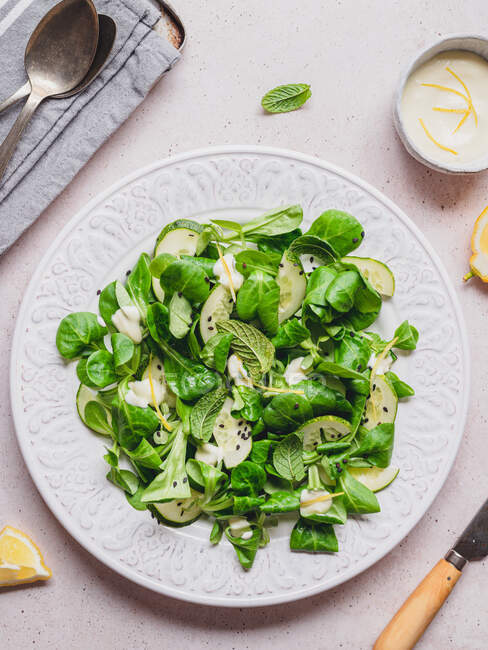 Вид зверху смачний зелений салат зі свіжими шматочками огірка та листям шпинату з чорним кунжутом проти лимонного соусу — стокове фото